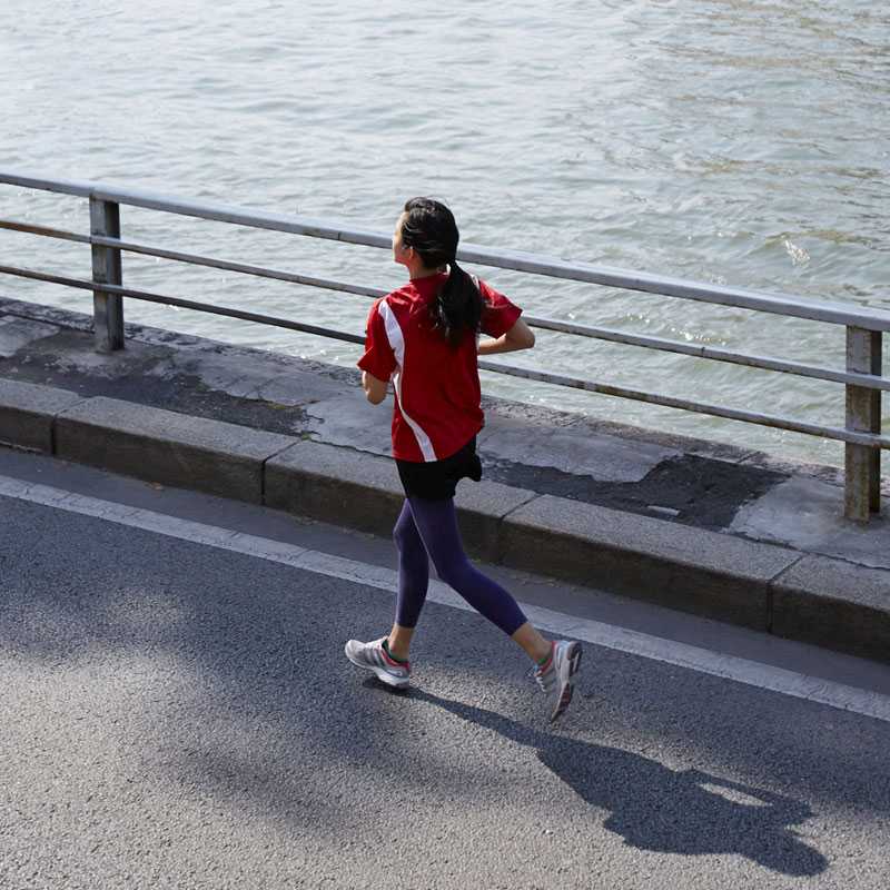 En kvinde løber langs en gade ved siden af vandet.