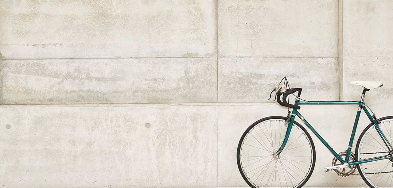 En turkis racercykel står op ad en grå betonvæg.