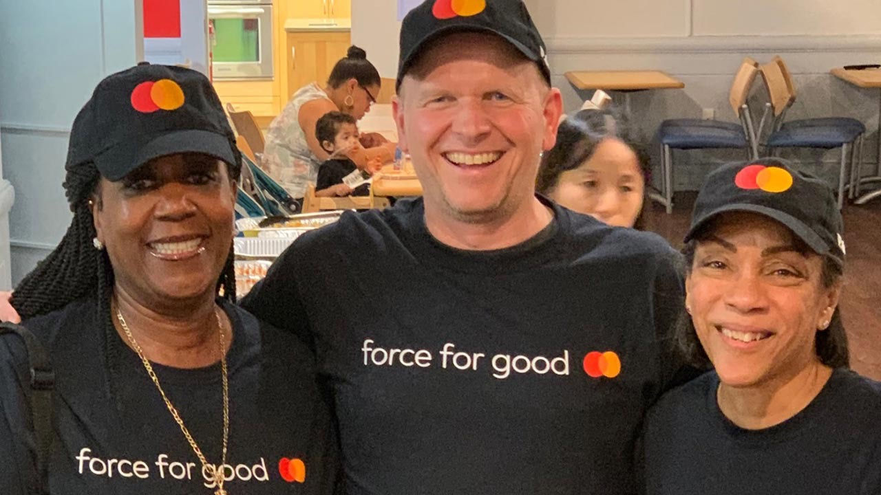 Tre smilende personer iført T-shirts og kasketter med Mastercard-logoet.