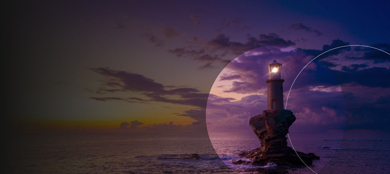 A lighthouse with a glowing light against a dramatic sunset sky.