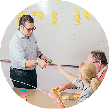 Man handing sticky notes to two colleagues at a table in a meeting room.