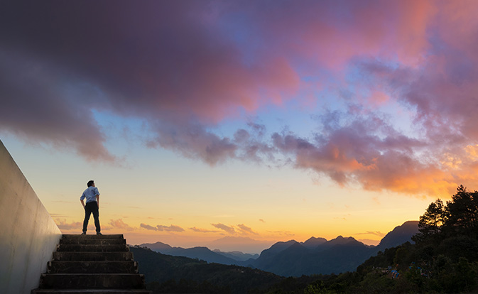 Businessman standing at top of stairs looking at sunset.