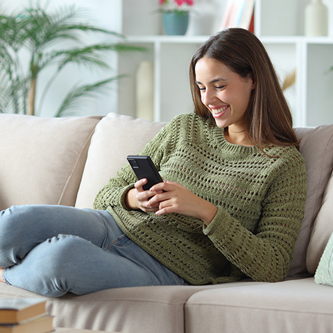 Woman using her smartphone while laying on the sofa