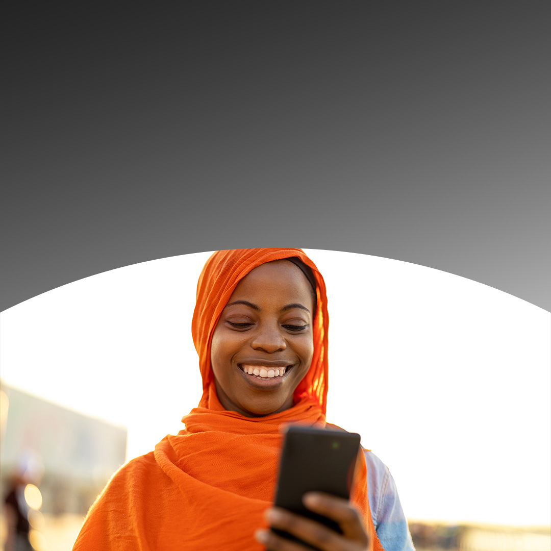 Woman in headscarf smiling at her smartphone.