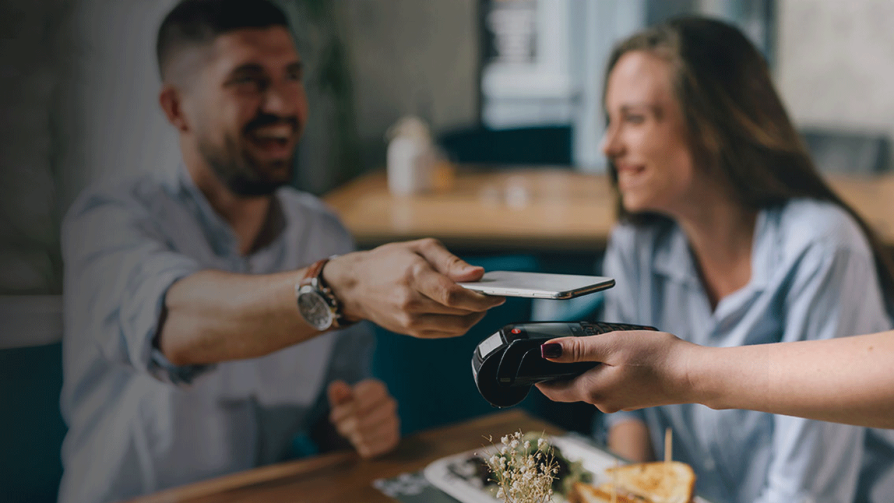 Man paying for food with mobile phone sitting next to woman