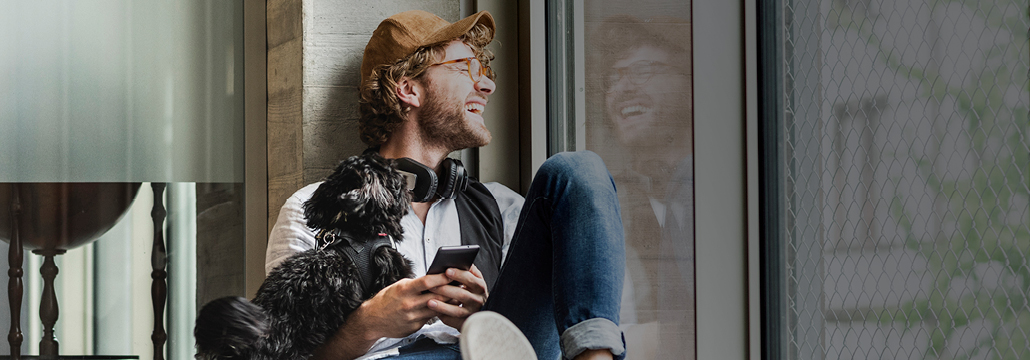 Man with dog and phone in hand looking through window