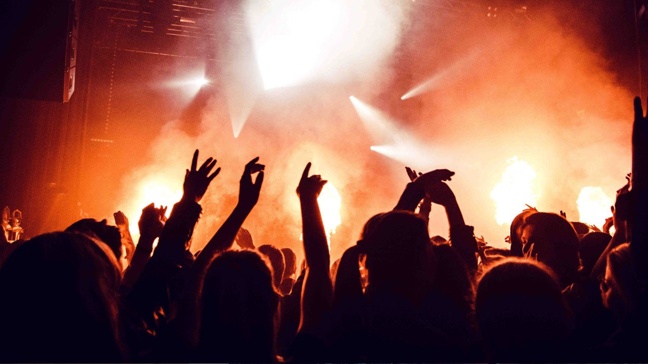 Music fans dance at a concert during a light show. 