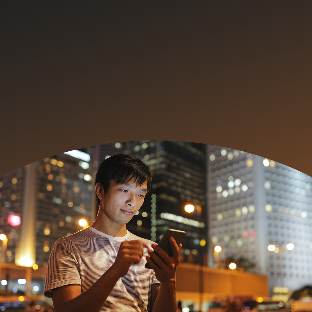 Un homme en ville, concentré sur son téléphone, qui est entouré de bâtiments urbains dans une ambiance très animée.