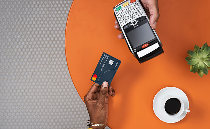 Un client tenant une carte Mastercard, prêt à payer avec un terminal de paiement à la table d'un café.