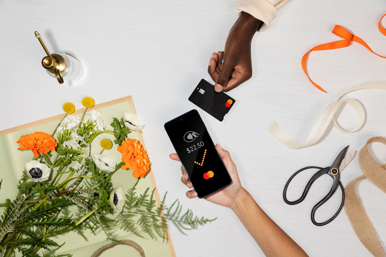 Hands exchanging a credit card, with one person holding a smartphone displaying a payment app..