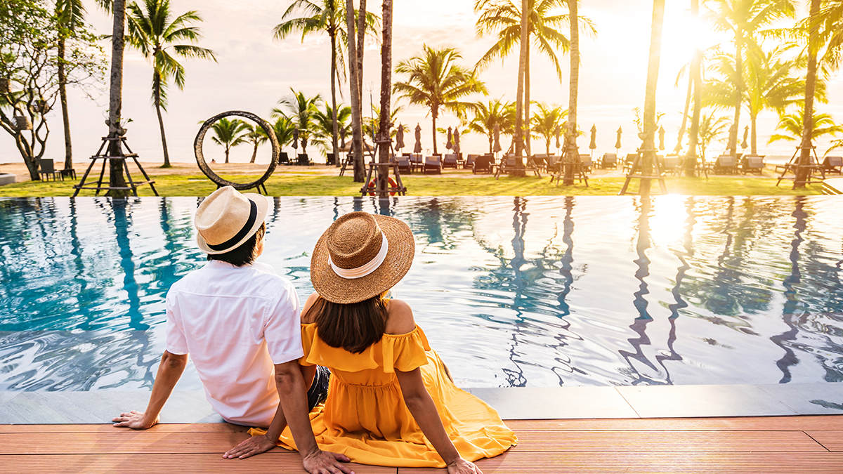 Two people with hats sitting poolside looking into the sun