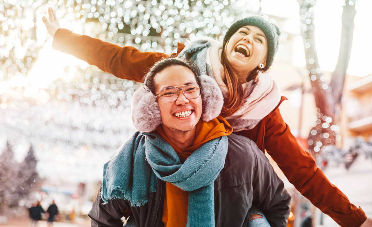 Multiracial couple in love wearing winter clothes celebrating Christmas holiday - Husband and wife having fun hanging out together walking on city street - Winter holidays and relationship concept