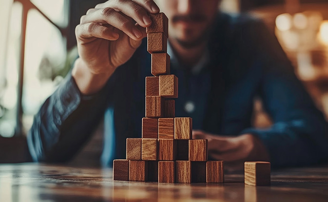 Hand placing a wooden block on top of a growing tower.