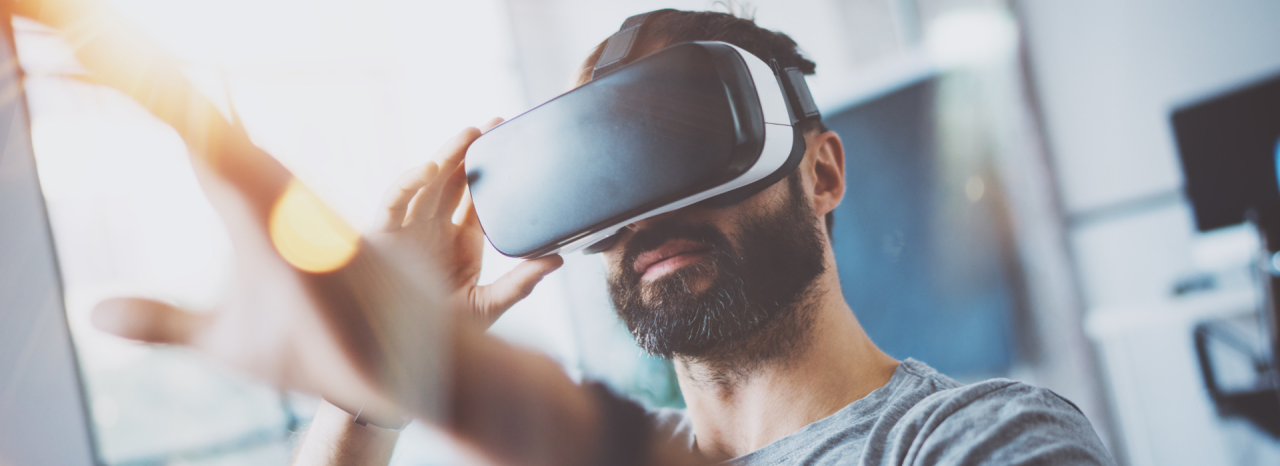 A man wearing virtual reality goggle holds his hand up. 