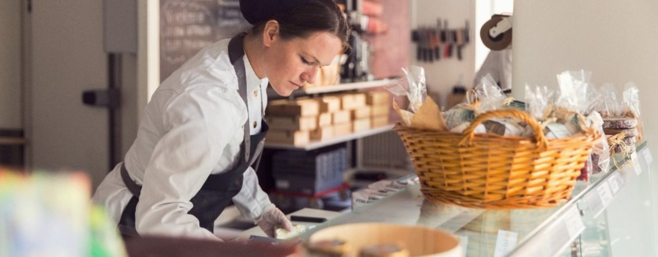 A business owner in an apron does some paperwork in front of a counter topped by baskets. 