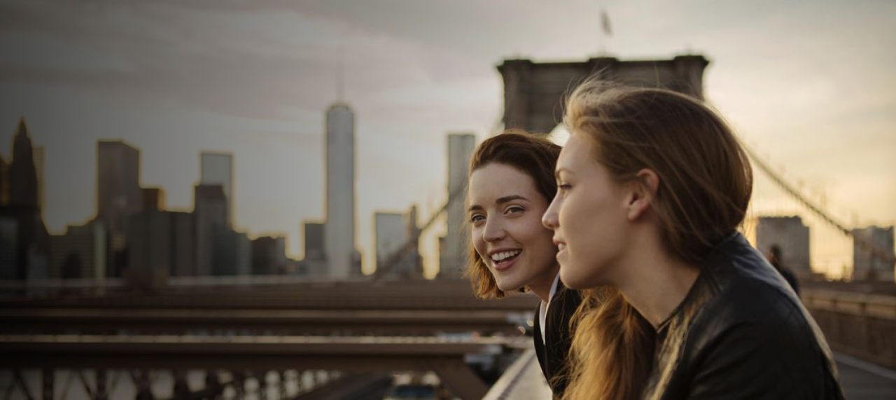 two women smiling near сity bridge