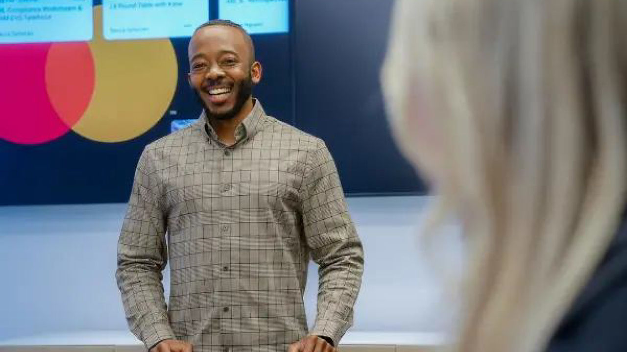 A man giving a presentation in front of a Mastercard logo.
