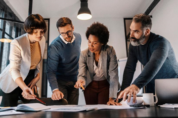 Group of people standing around table working collaboratively. 
