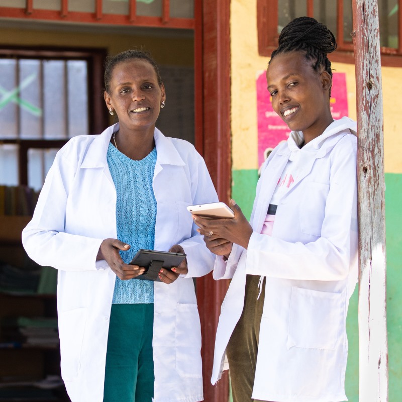 Two community health workers in Ethiopia hold tablets outside a clinic. 