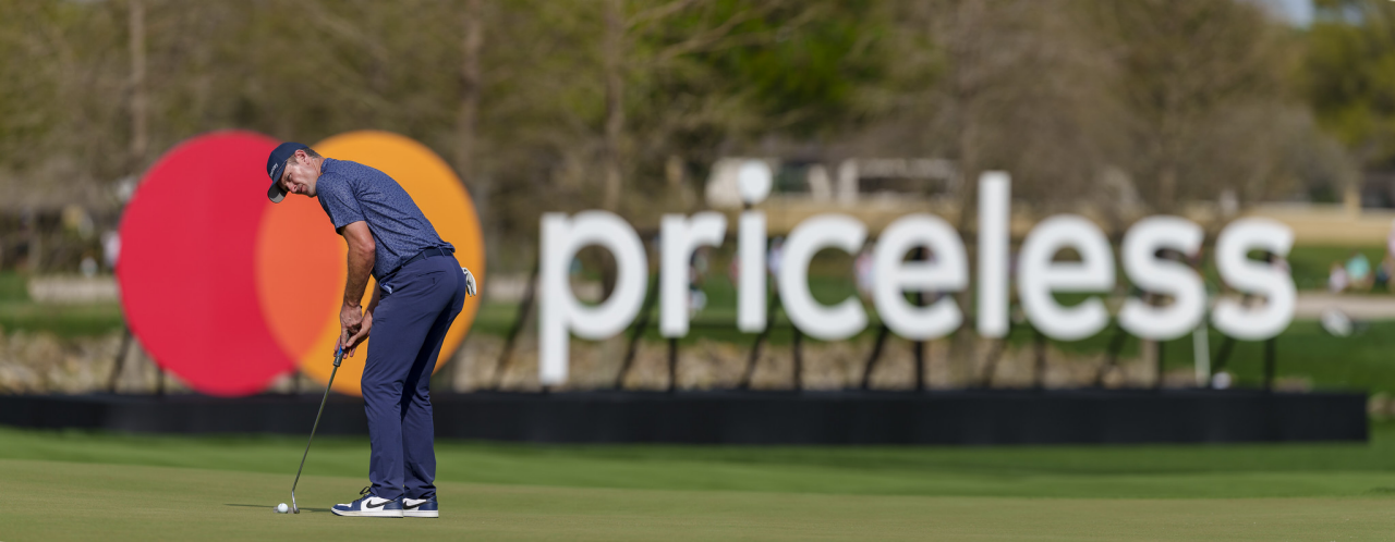 Justin Rose 在萬事達卡標誌和 Priceless 標誌前的果嶺上排成擊球線。 