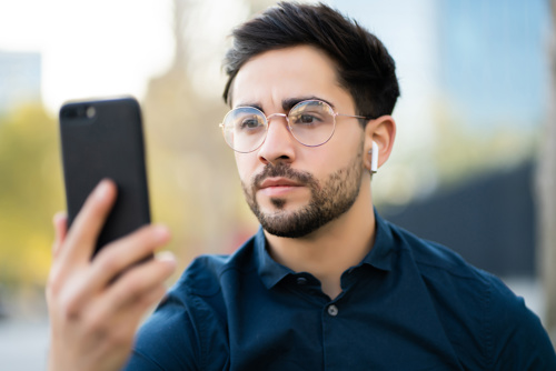 Portrait of young man using face id for unlock mobile phone while standing outdoors. Technology concept.