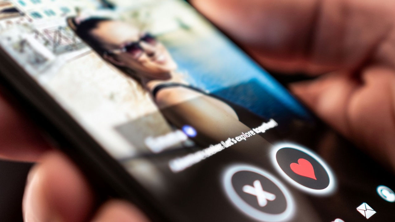 A person holds a smartphone with a dating app open on it. 