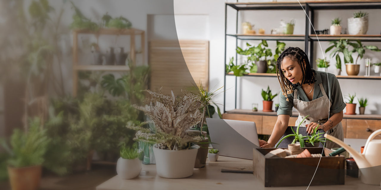 Una donna concentrata sul suo laptop, circondata da piante in un allegro negozio di piante.