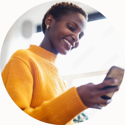 黄色いセーターを着た女性がスマートフォンを見て微笑んでいる。