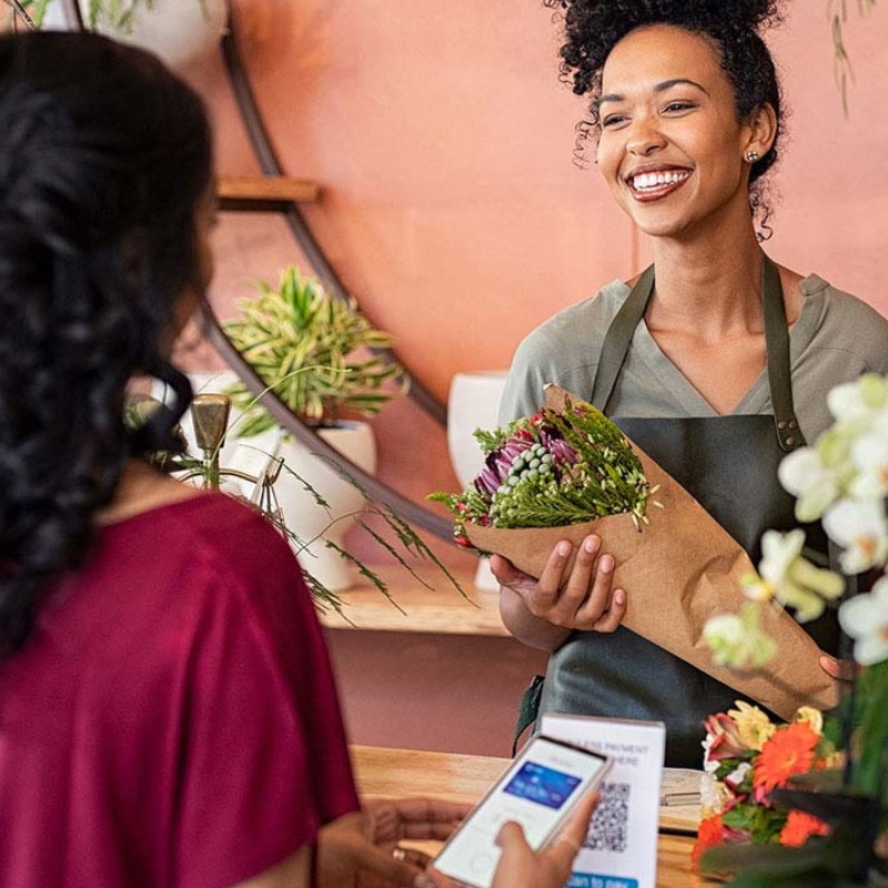 A florist holds a bouquet while a woman pays via mobile wallet. 