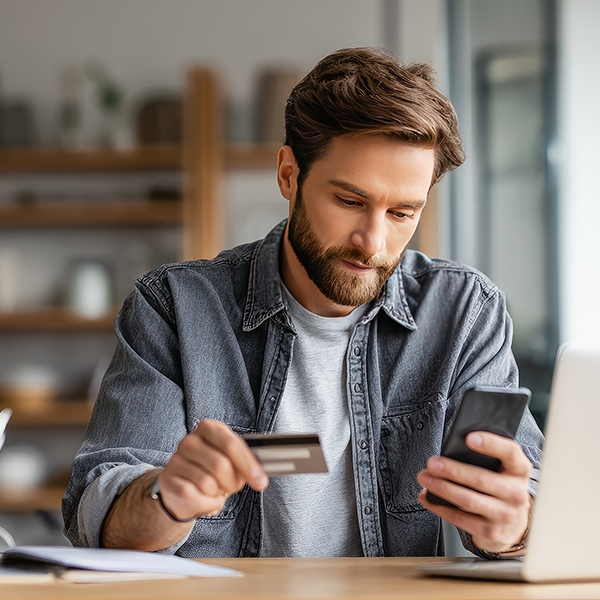 A man looks at his phone and holds his credit card. 