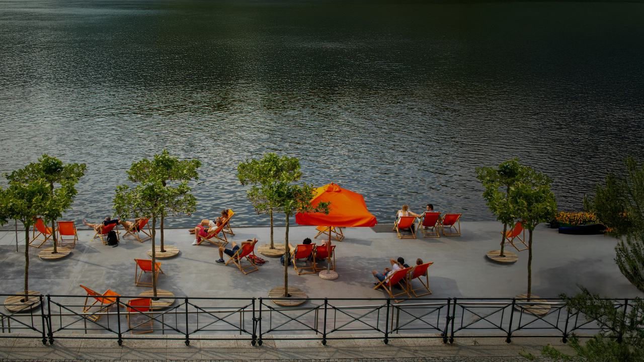 People sit on orange chairs on a large patio overlooking a lake. 