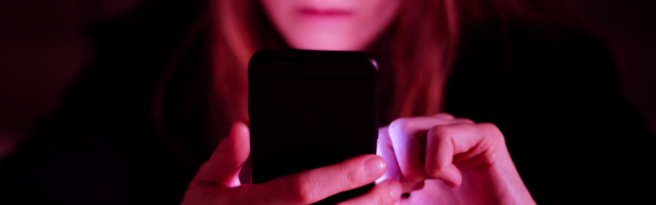 A woman looks at a smart phone emitting a pink glow. 