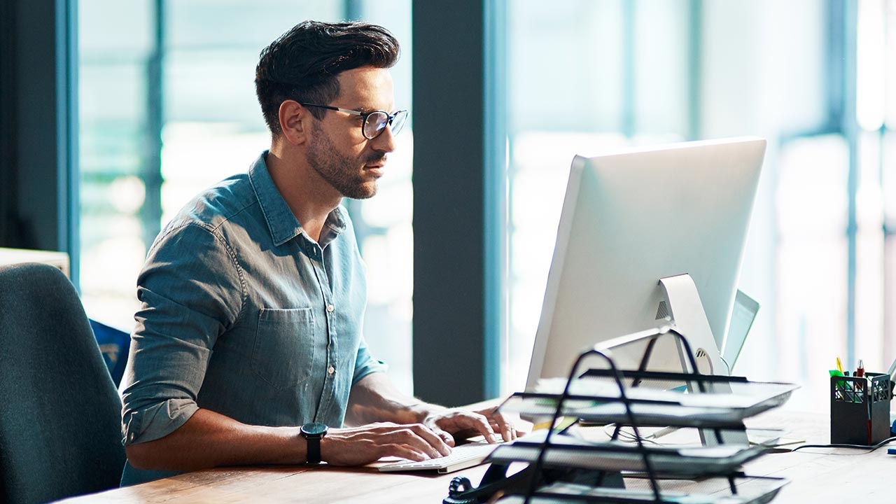 Joven empresario concentrado usando la computadora en su escritorio en una oficina moderna.