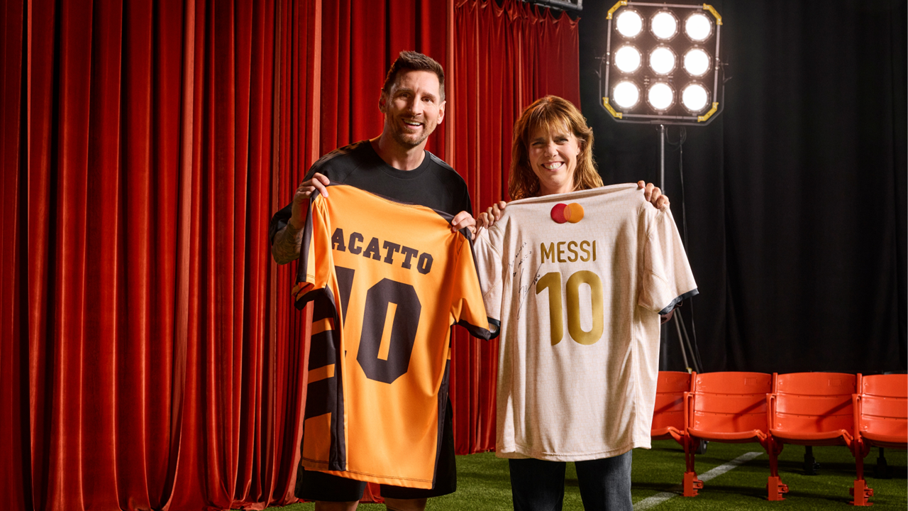 Lionel Messi and a happy fan posing together on a stage set. Messi holds a purple and pink "Mammo 19" jersey, while the fan holds a white and red signed "Messi 30" jersey featuring the MasterCard logo.