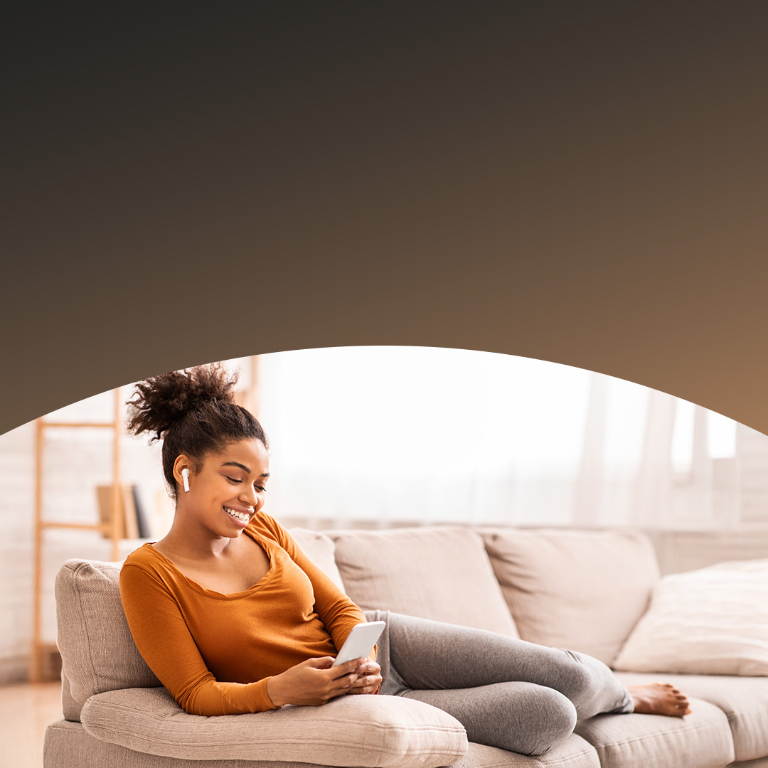Femme lisant sur son téléphone assise sur son canapé. 