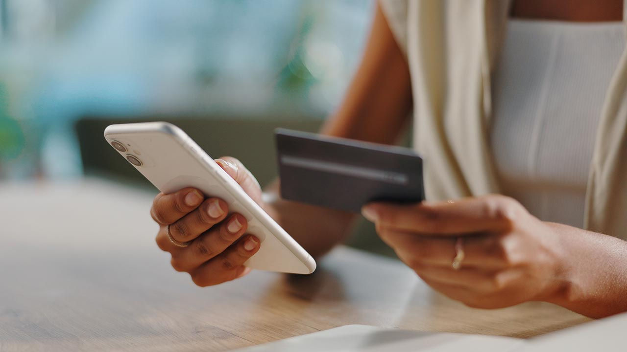 Persoană care ține telefonul și cardul de credit.