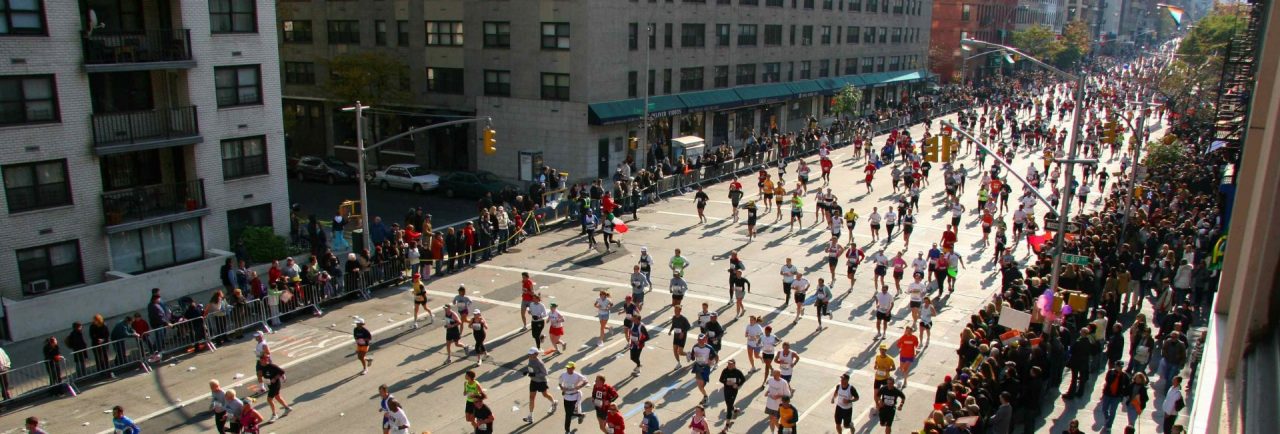 Alergătorii de la Maratonul din New York se derulează pe o stradă a orașului, în timp ce oamenii îi aplaudă pe margine.