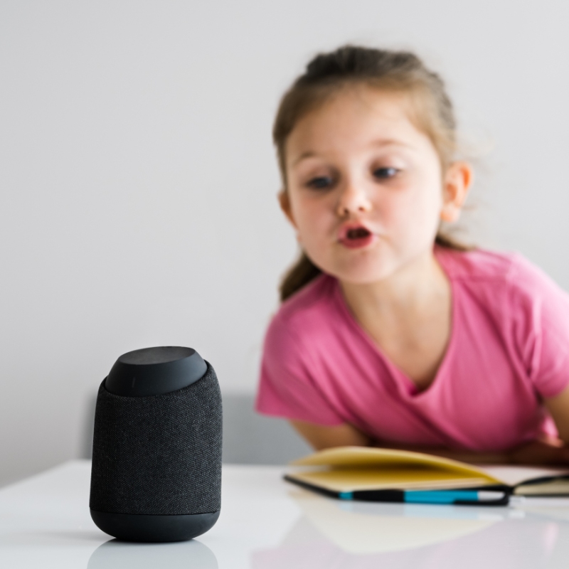 A young girl talks to a smart speaker.