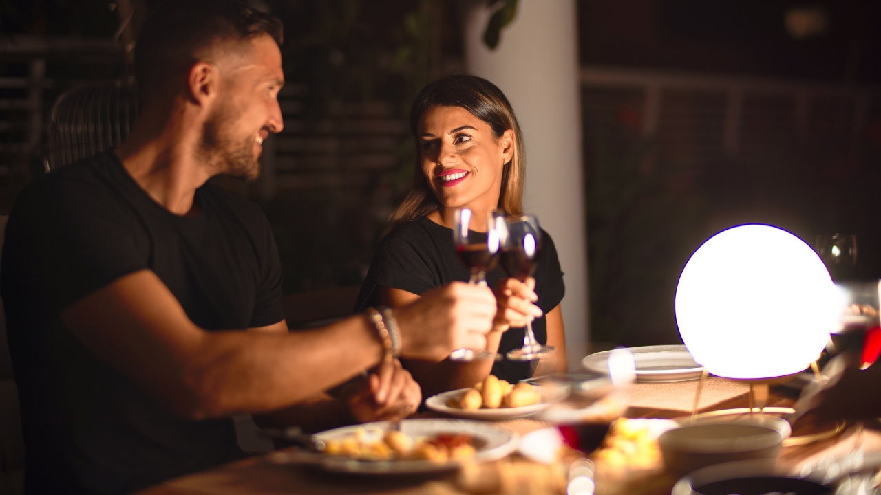 A man and a woman raise their glasses of wine to each other at a romantic restaurant. 