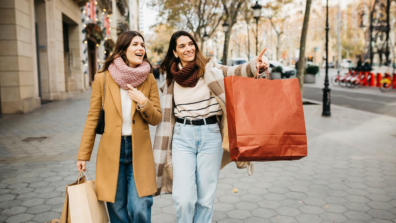 две женщины идут по городской улице с сумками для покупок