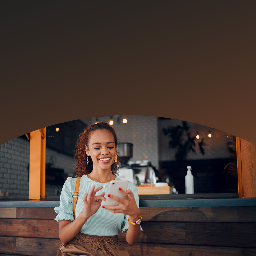 فتاة تقوم بإجراء عملية دفع باستخدام هاتفها الذكي أثناء وقوفها عند طاولة مقهى.