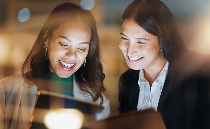 two women smiling while shopping on a tablet