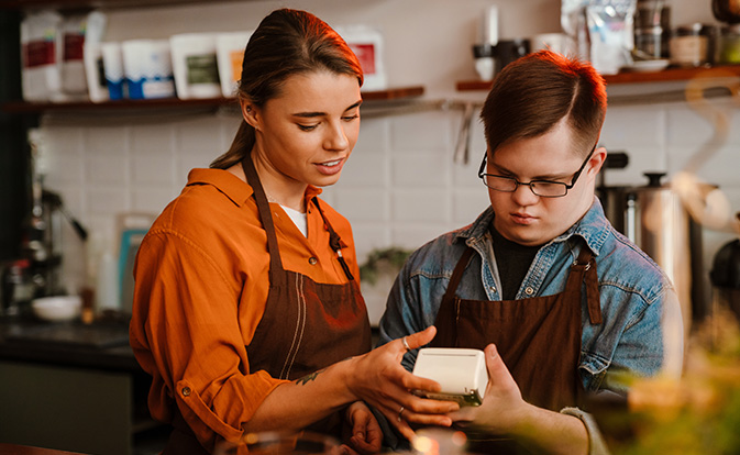 Two restaurant staff in aprons examine a transaction in progress on a card payment terminal.