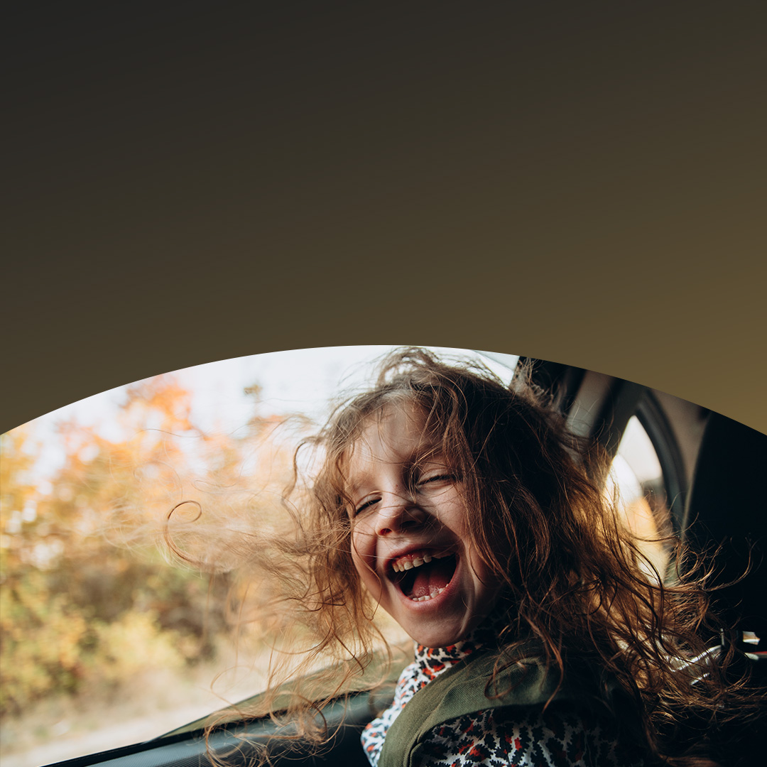 Enfant aux cheveux longs riant joyeusement sur le siège arrière d'une voiture