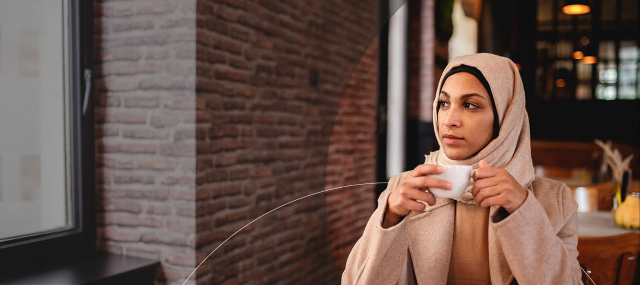 une femme portant un hijab tenant une tasse de café.