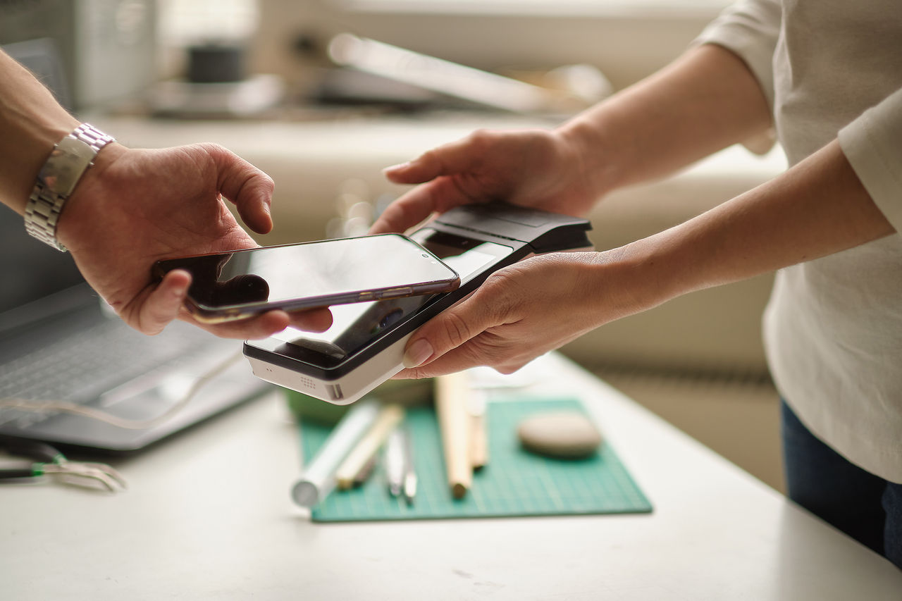 Person makes a contactless payment by tapping a mobile phone on a POS terminal held by another.