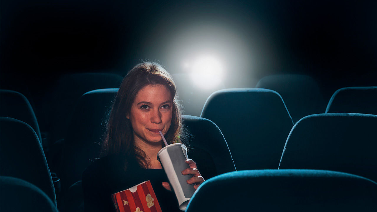 Una mujer disfrutando de una película en el cine bebiendo refresco. 