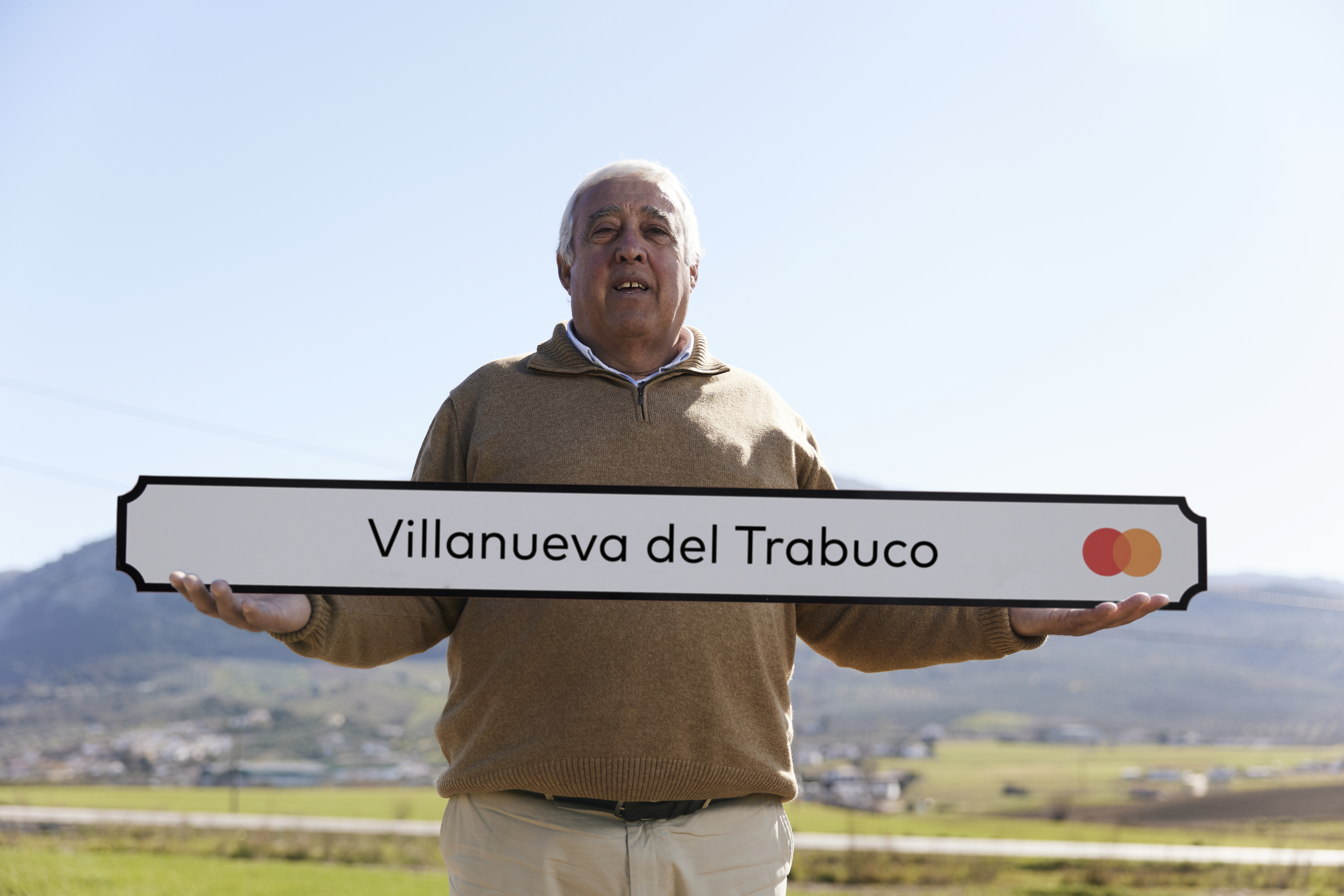 El alcalde de Villanueva del Trabuco (Málaga), D. Juan Luis Gallardo, posa mostrando un cartel con el nombre de su pueblo.