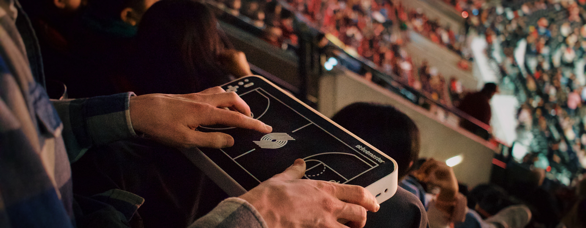 A basketball fan holds a haptic-enable tablet that syncs with game play in the stands at a game.