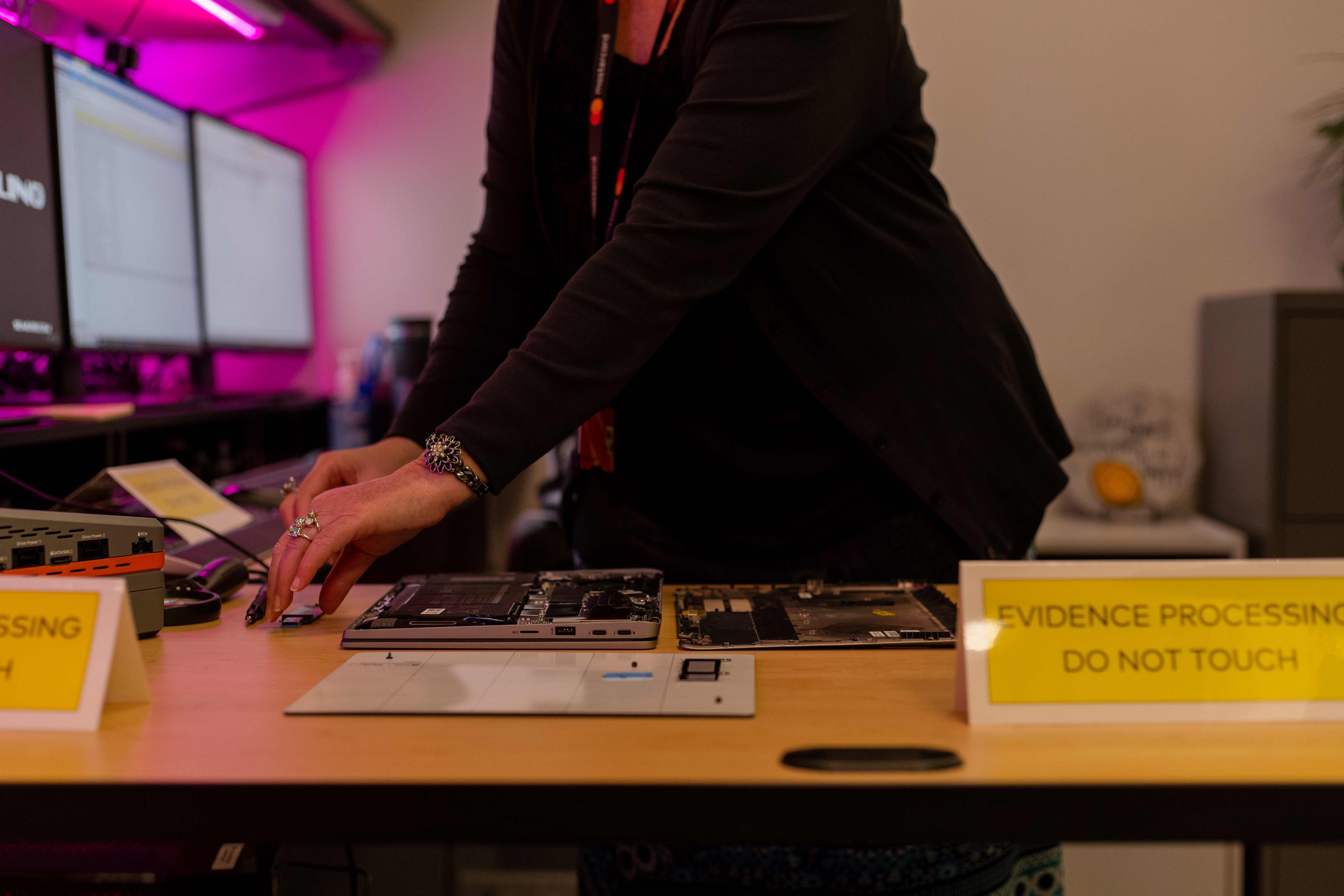 A woman handles the innards of a computer in an evidence processing lab.